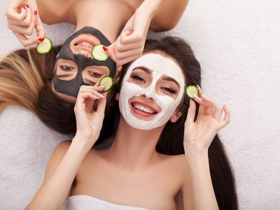 A picture of two girls friends relaxing with facial masks on over white background.