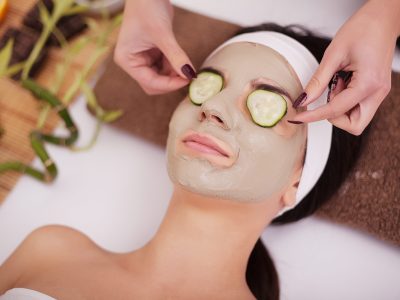 Woman with clay facial mask in beauty spa. In background tropical plants