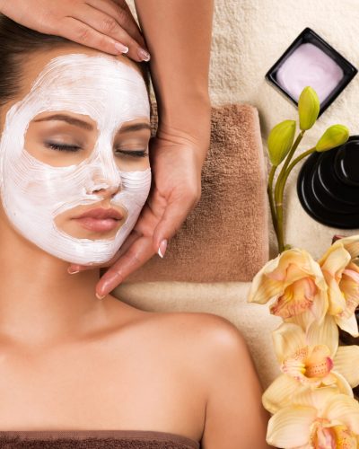 Beautiful woman with mask on her face having head massage in the spa salon.